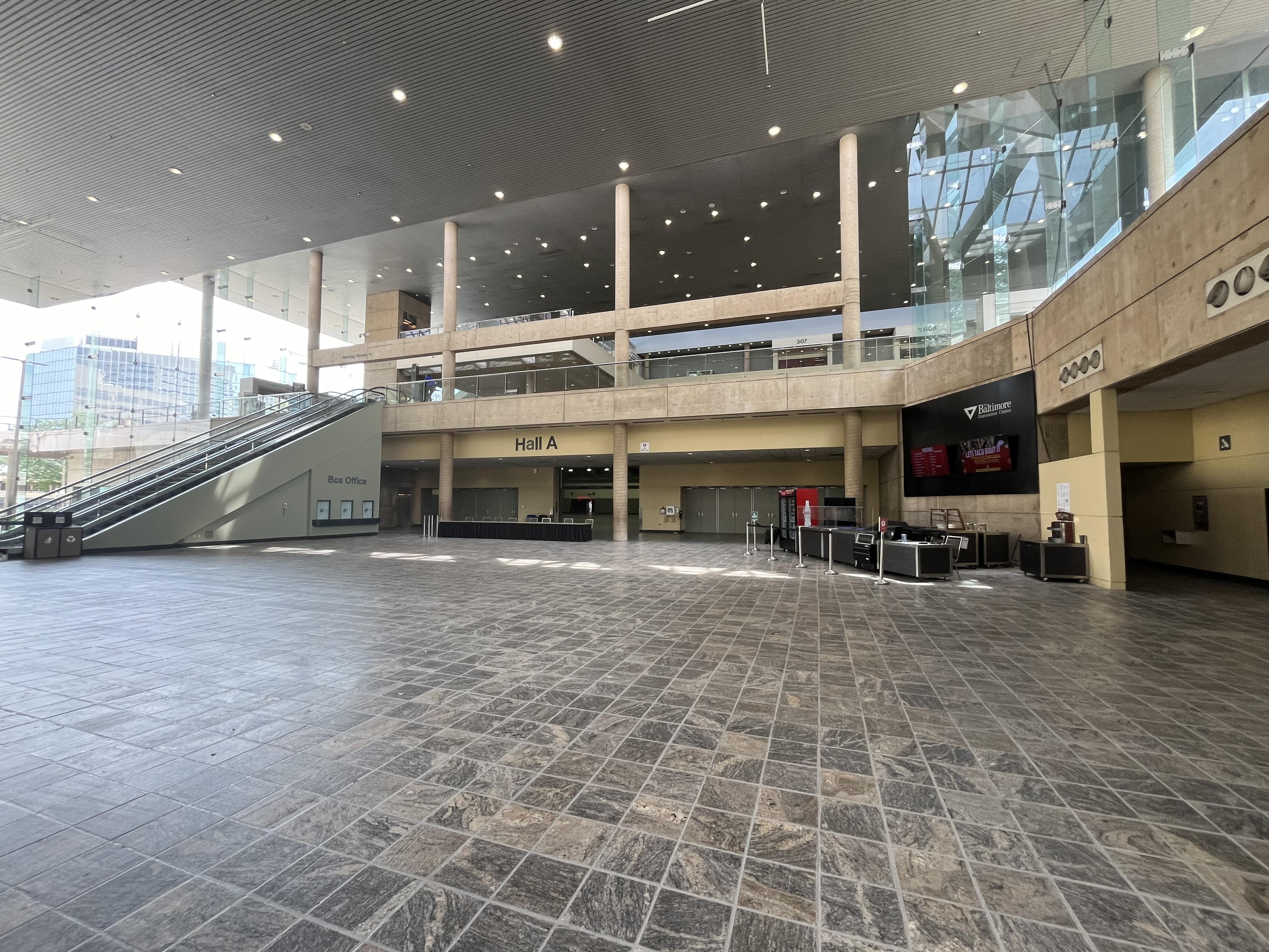 The Charles Street Lobby is a large lobby with many windows letting in a lot of natural light. The flooring is a gray square tile. To the left of this photo is an escalator that goes to Level 200. Hall A is shown here, which is the Bookfair exit. To the right is Hall C, the main Bookfair entry.