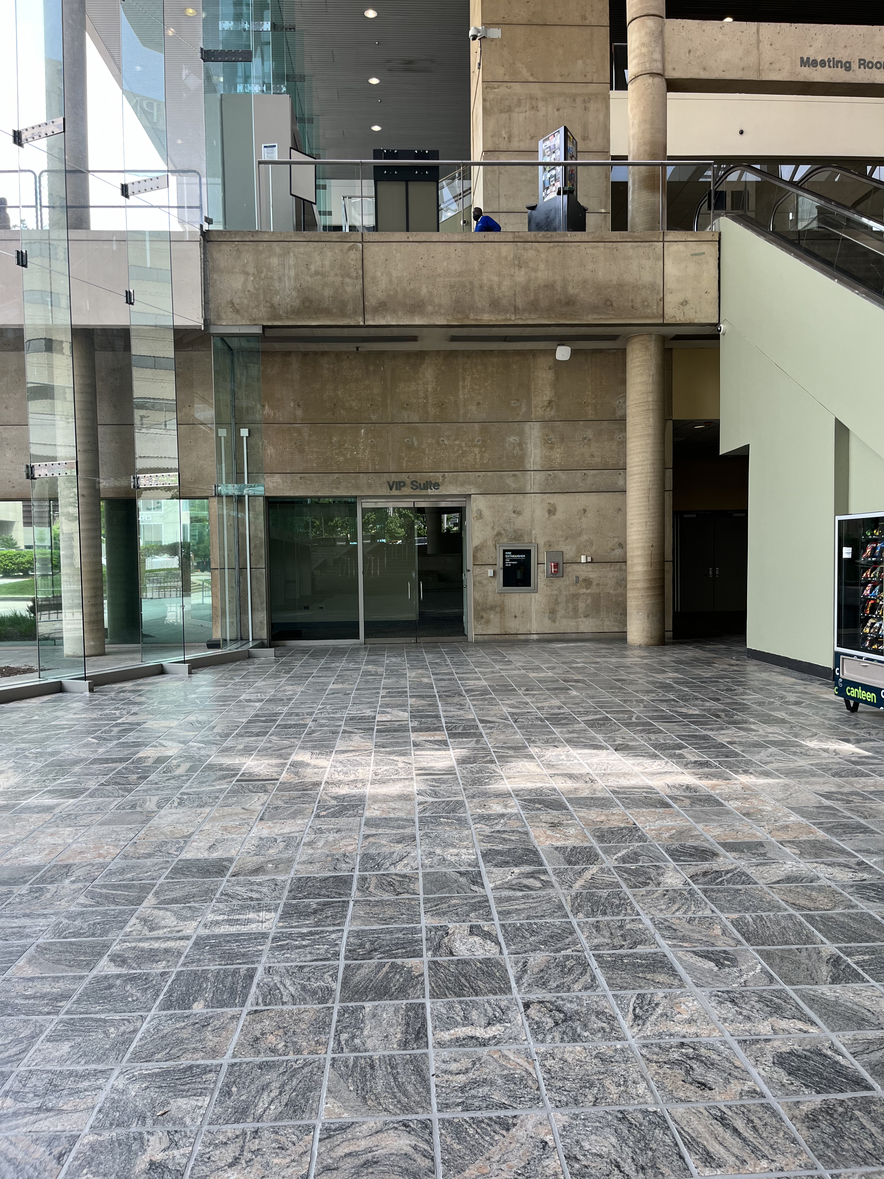 The photo is taken from directly inside the Charles Street lobby entrance. To the left is a glass wall to the outside, to the right is an escalator to Level 200, and in between is a large empty space where the Accessibility Desk will be located.