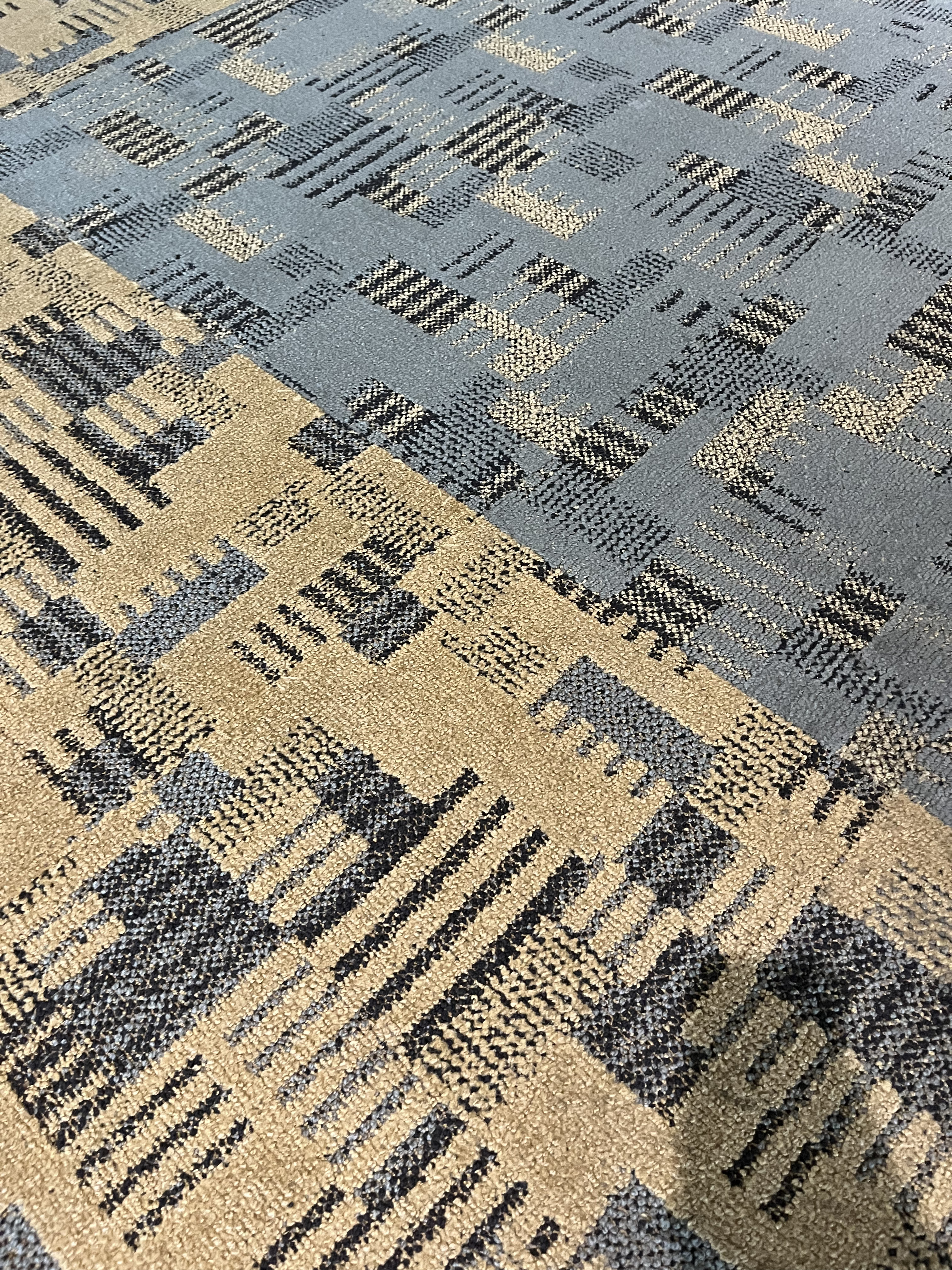 A close-up of the carpet, which is a block and stripe pattern in a grayish blue, black, beige, and yellow pattern.