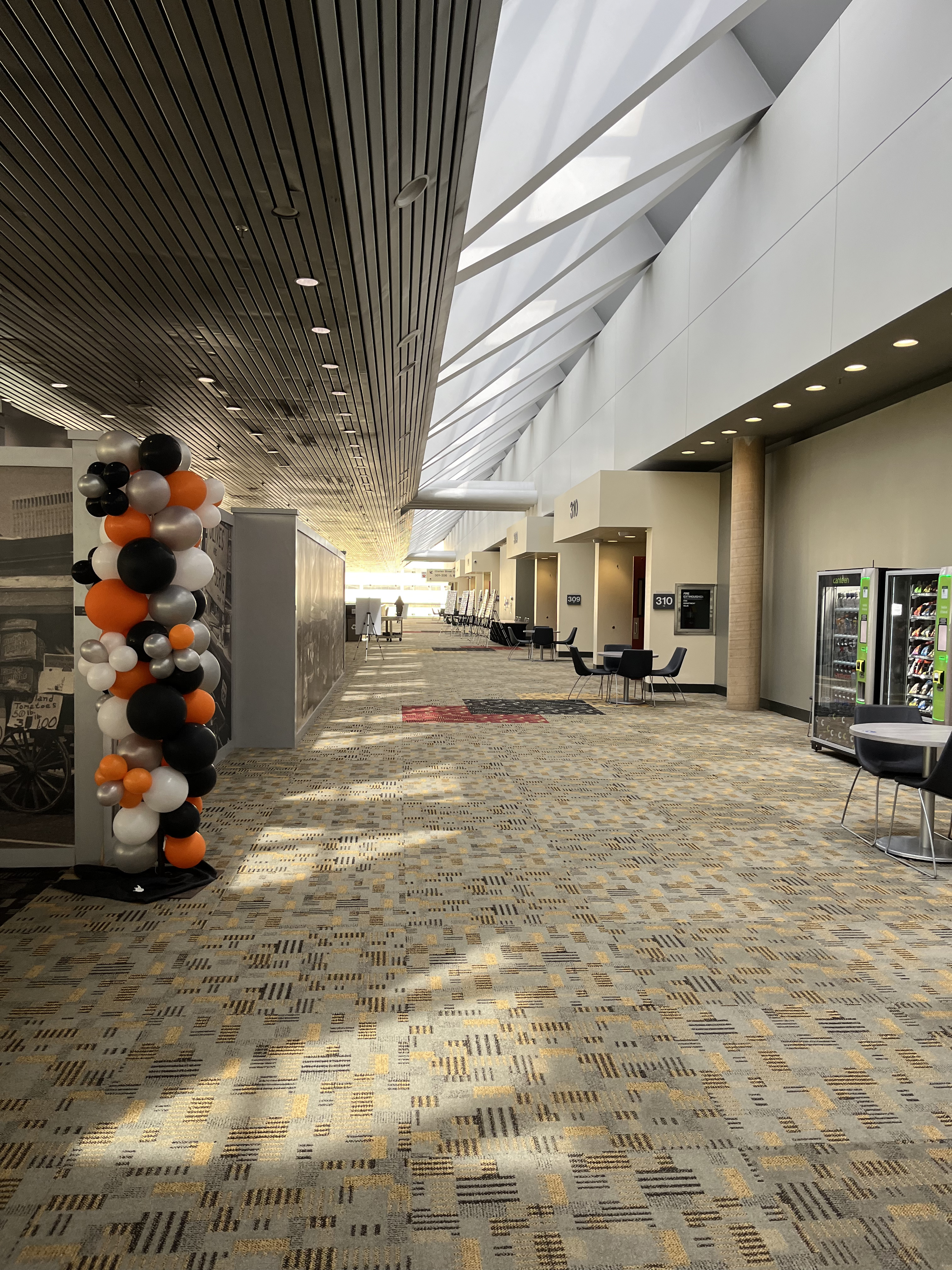 A picture of the Level 300 hallway with the escalator entry on the left of the photo and meeting rooms on the right. There are some small table rounds with chairs placed along the right side of the hallway as well.