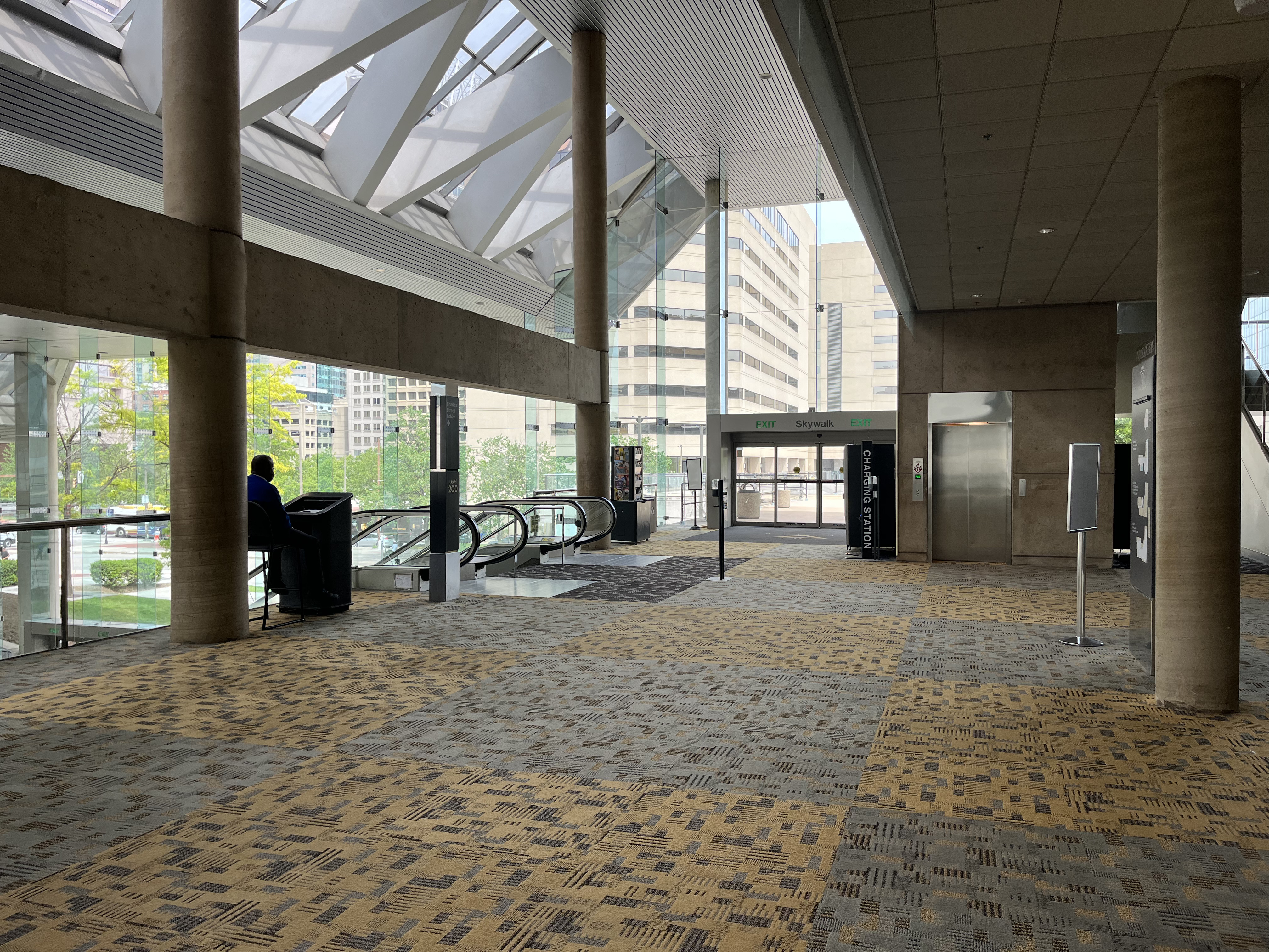 This photo shows a mezzanine hallway on Level 200. To the left in this photo are the escalators from Level 100 and on the right is an elevator that accesses level 100, 200, and 300. The flooring is a hard-pile carpet in grayish-blue and yellow block pattern.