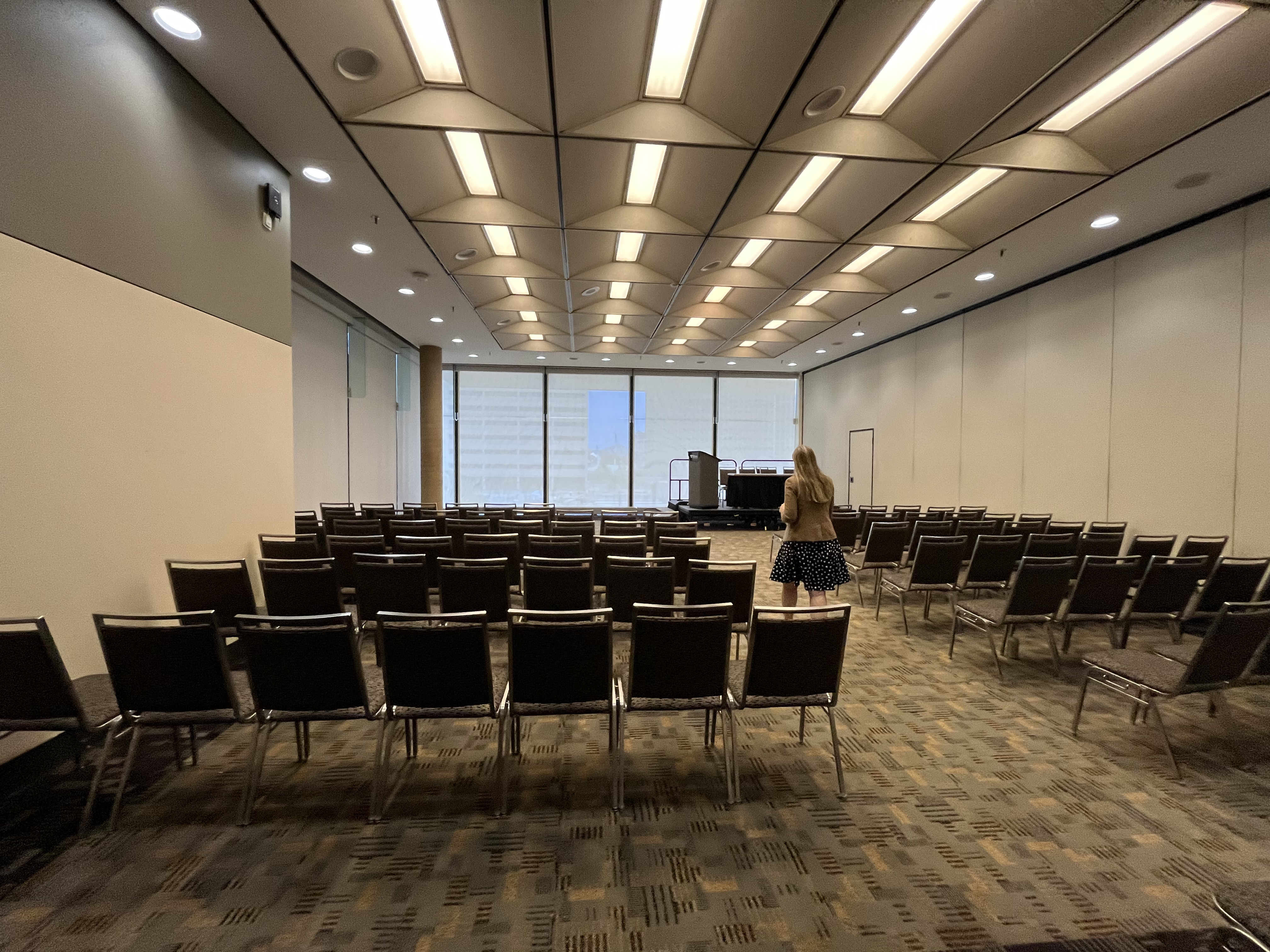 A photo taken at the entrance of a meeting room in the Baltimore Convention Center with the same carpet as the hallway. Gray and metal chairs are set in rows with a center aisle.